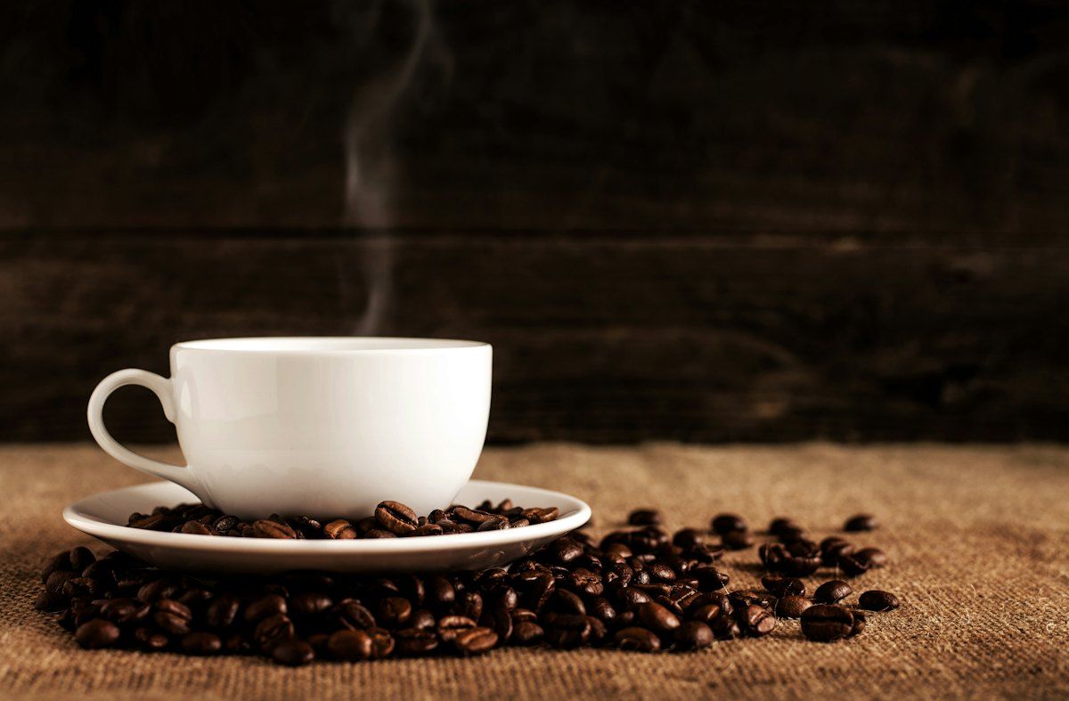 Steaming cup of dark roast coffee with beans on a wooden table